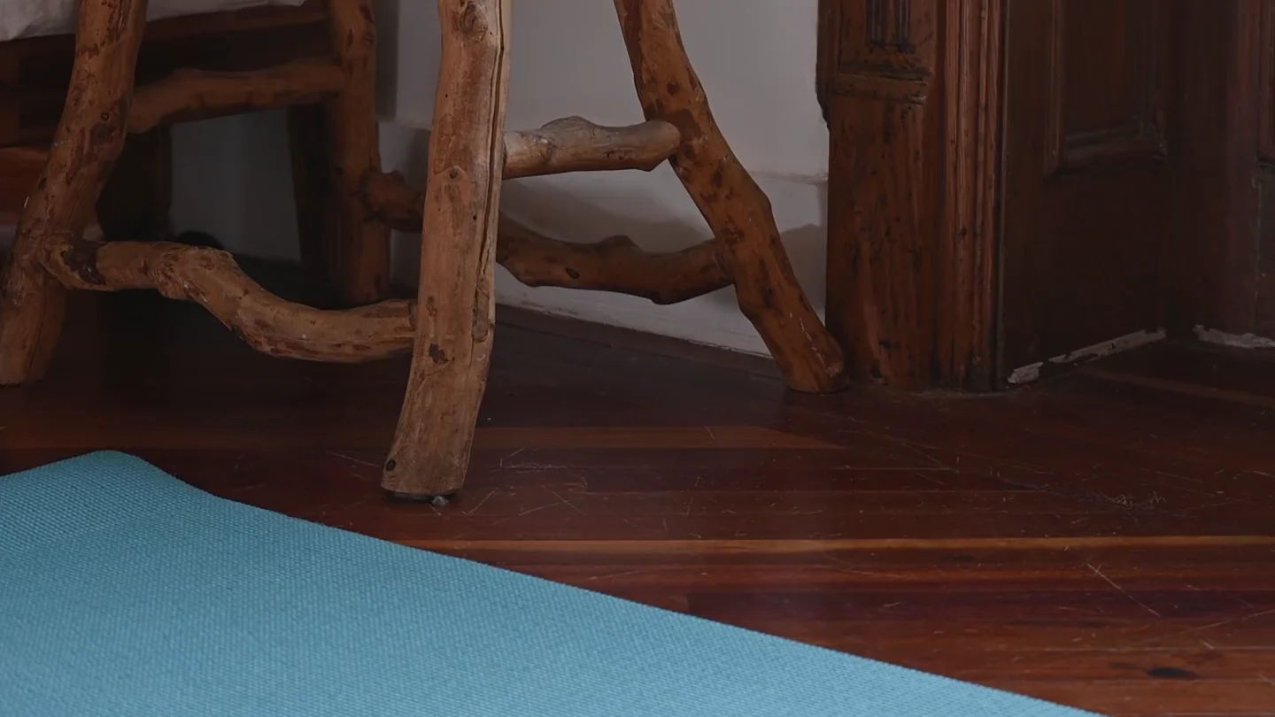 A blue exercise mat on a wooden floor beside a stool and potted plant.