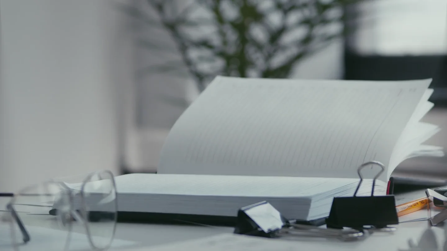 An open notebook on a desk with stationery and a plant nearby.